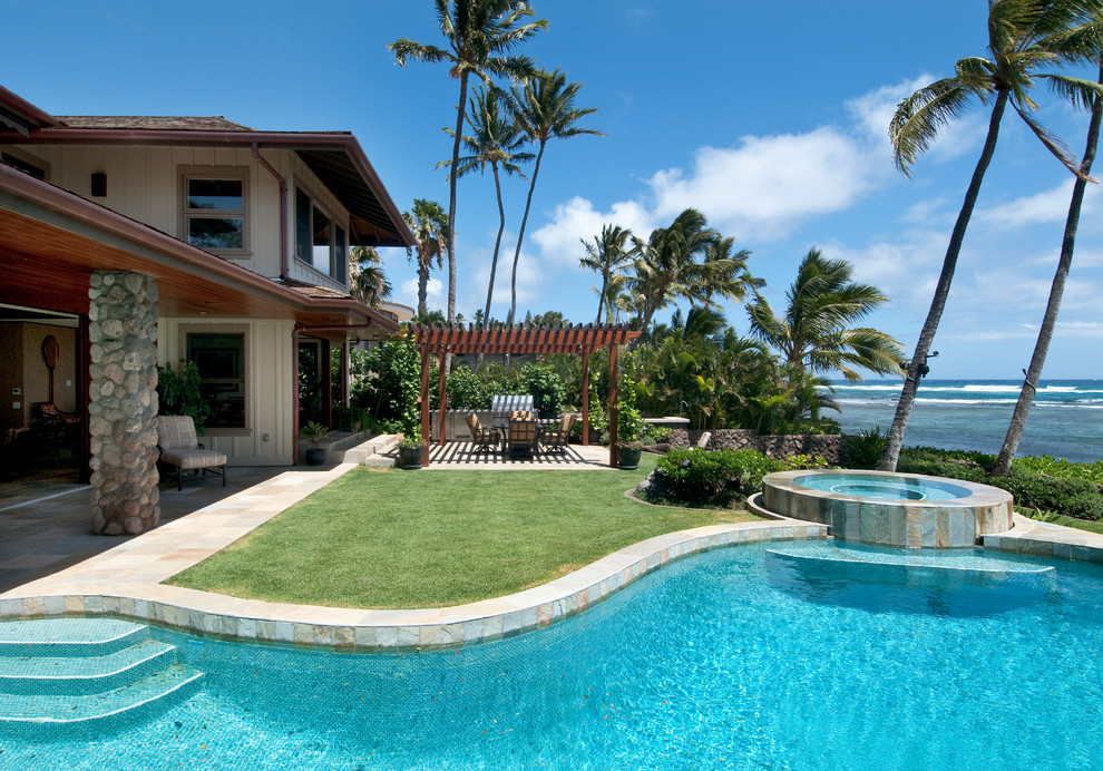 Large tropical backyard custom-shaped pool in Hawaii with a hot tub.