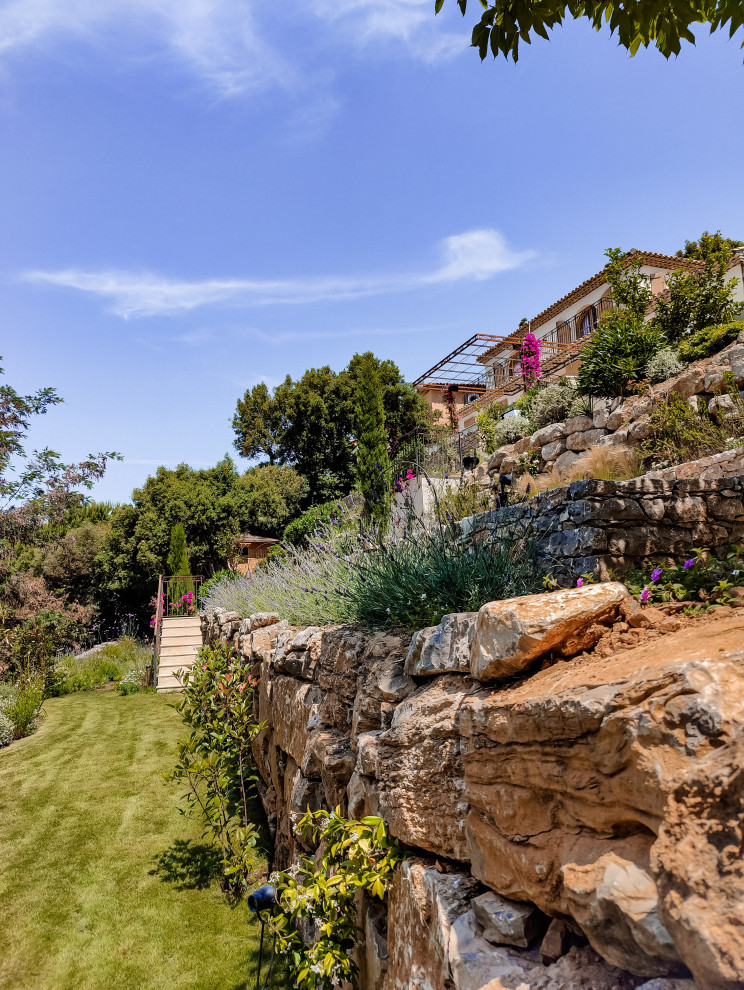 This is an example of a medium sized mediterranean sloped full sun garden in Other with a flowerbed.