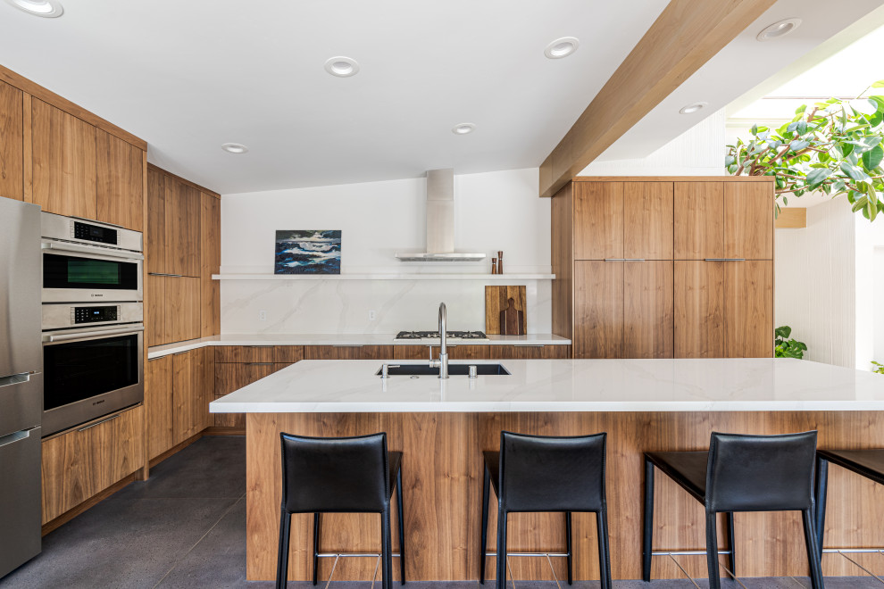 This is an example of a contemporary u-shaped eat-in kitchen in Sacramento with an undermount sink, flat-panel cabinets, medium wood cabinets, white splashback, engineered quartz splashback, stainless steel appliances, cement tiles, with island, grey floor, white benchtop and exposed beam.