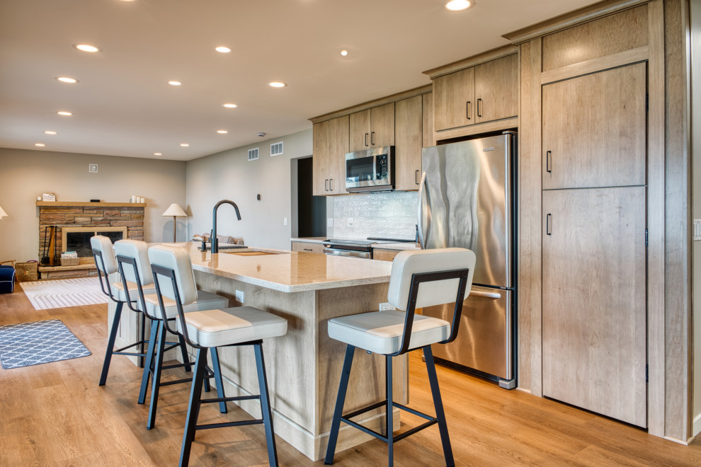 Inspiration for a mid-sized transitional galley vinyl floor and brown floor open concept kitchen remodel with an undermount sink, flat-panel cabinets, light wood cabinets, quartz countertops, white backsplash, subway tile backsplash, stainless steel appliances, an island and white countertops