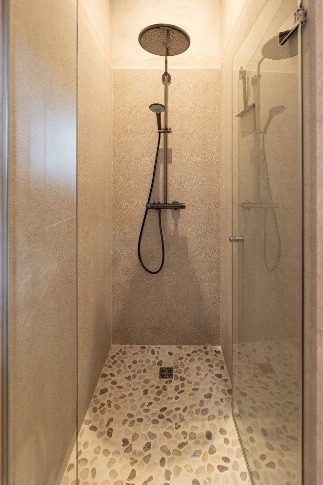 На фото: ванная комната в средиземноморском стиле с душем без бортиков, бежевой плиткой, плиткой из травертина, полом из галечной плитки, бежевым полом и открытым душем