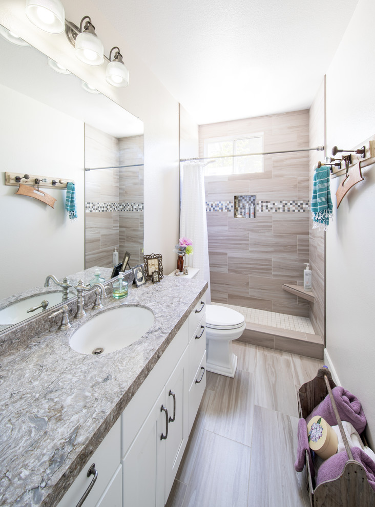 This is an example of a mid-sized transitional 3/4 bathroom in San Francisco with recessed-panel cabinets, white cabinets, an alcove shower, a two-piece toilet, gray tile, porcelain tile, grey walls, porcelain floors, an undermount sink, engineered quartz benchtops, white floor, a shower curtain and brown benchtops.