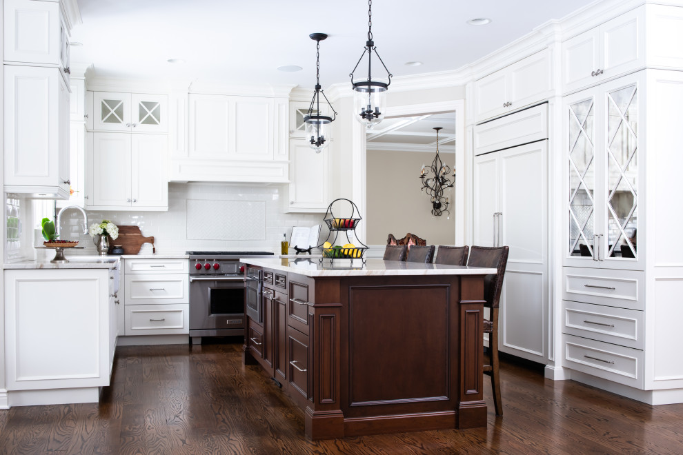 Photo of a large traditional u-shaped kitchen in New York with a farmhouse sink, beaded inset cabinets, white cabinets, white splashback, subway tile splashback, stainless steel appliances, dark hardwood floors, with island, brown floor and white benchtop.
