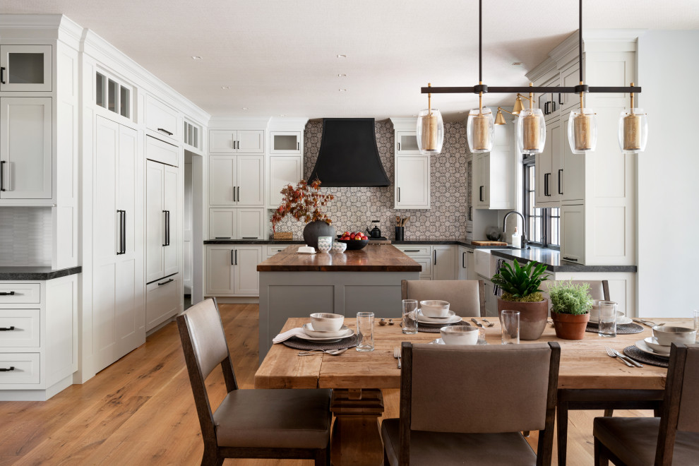 Design ideas for a large traditional l-shaped kitchen/diner in Other with a belfast sink, shaker cabinets, white cabinets, wood worktops, multi-coloured splashback, white appliances, light hardwood flooring, an island and brown worktops.