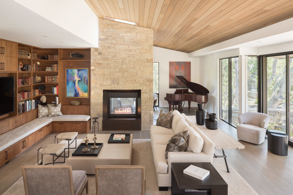 Mid-sized contemporary enclosed living room in San Francisco with a music area, white walls, light hardwood floors, a two-sided fireplace, a stone fireplace surround, a wall-mounted tv and brown floor.