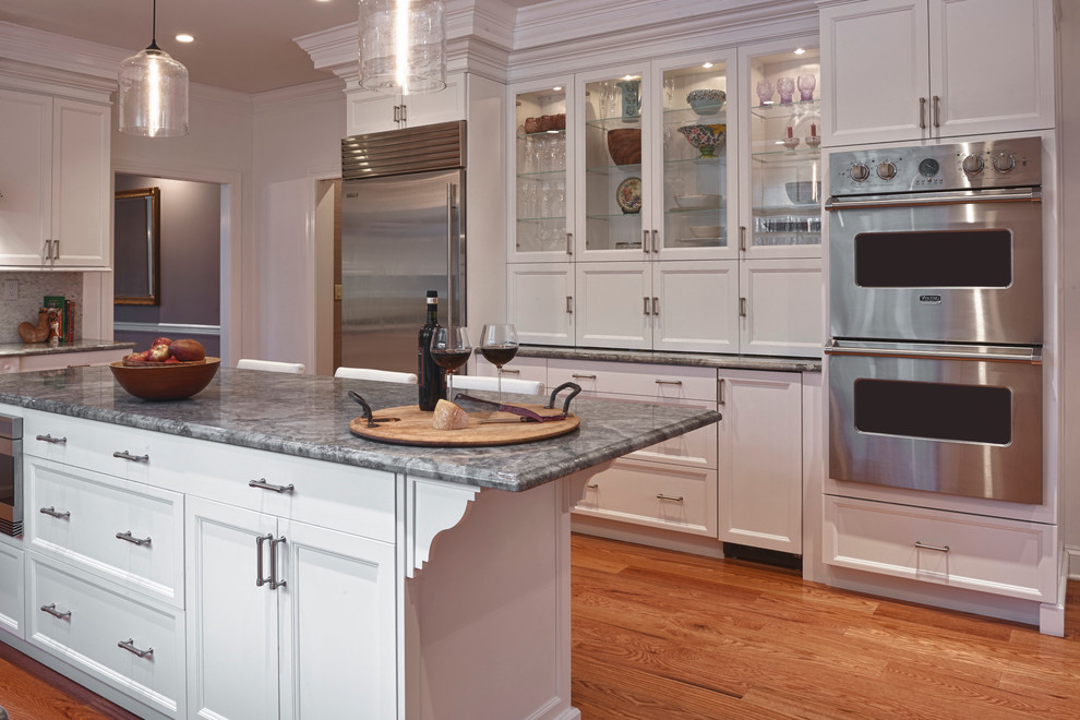 Example of a large transitional medium tone wood floor kitchen pantry design in New York with a farmhouse sink, shaker cabinets, white cabinets, quartzite countertops, white backsplash, mosaic tile backsplash, stainless steel appliances, white walls and an island