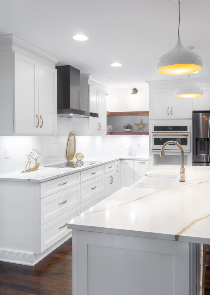 Design ideas for a mid-sized midcentury l-shaped open plan kitchen in Atlanta with a farmhouse sink, shaker cabinets, white cabinets, quartz benchtops, white splashback, porcelain splashback, stainless steel appliances, dark hardwood floors, with island, brown floor and white benchtop.