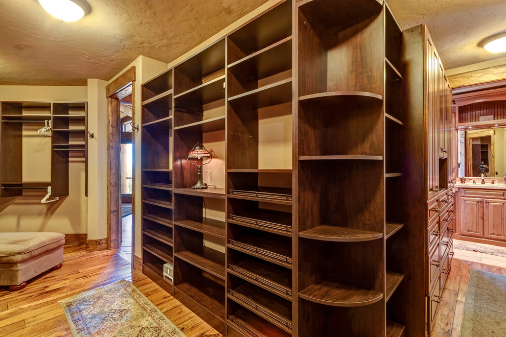 This is an example of a large country gender-neutral walk-in wardrobe in Denver with open cabinets, dark wood cabinets, medium hardwood floors and brown floor.