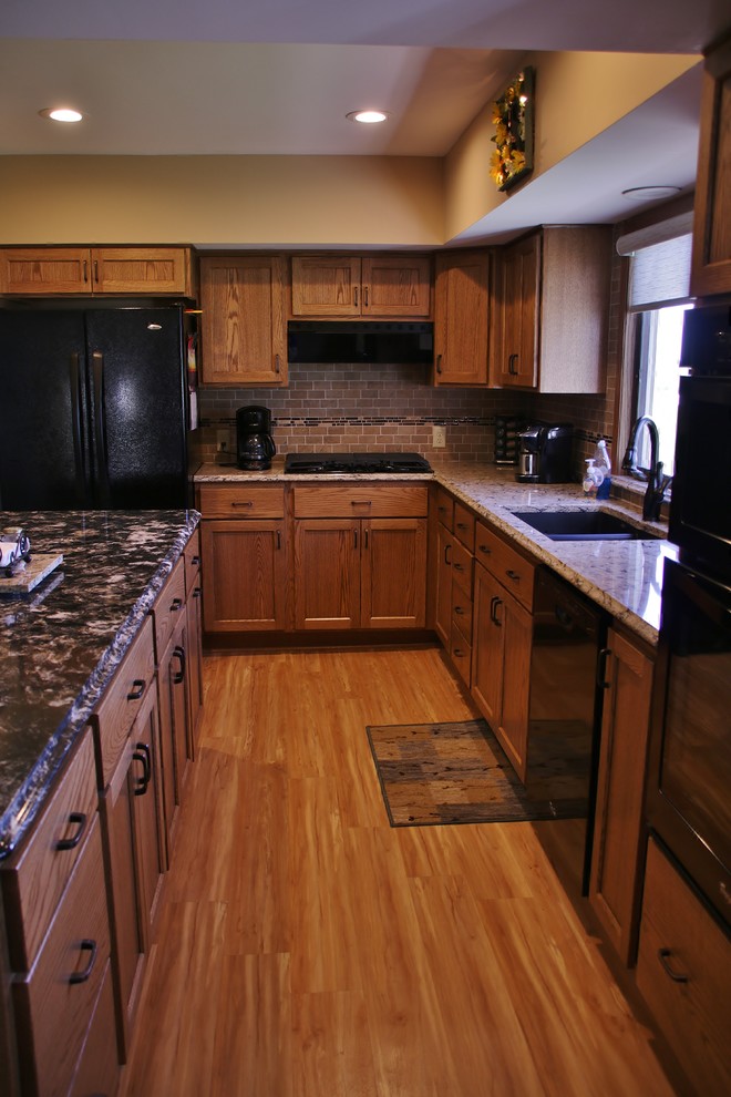 Example of a mid-sized l-shaped eat-in kitchen design with flat-panel cabinets, medium tone wood cabinets, quartz countertops, beige backsplash, black appliances and an island