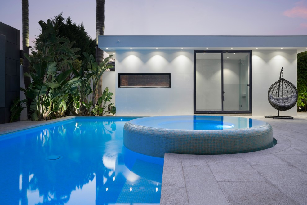 This is an example of a large modern backyard rectangular lap pool in Melbourne with a hot tub and natural stone pavers.
