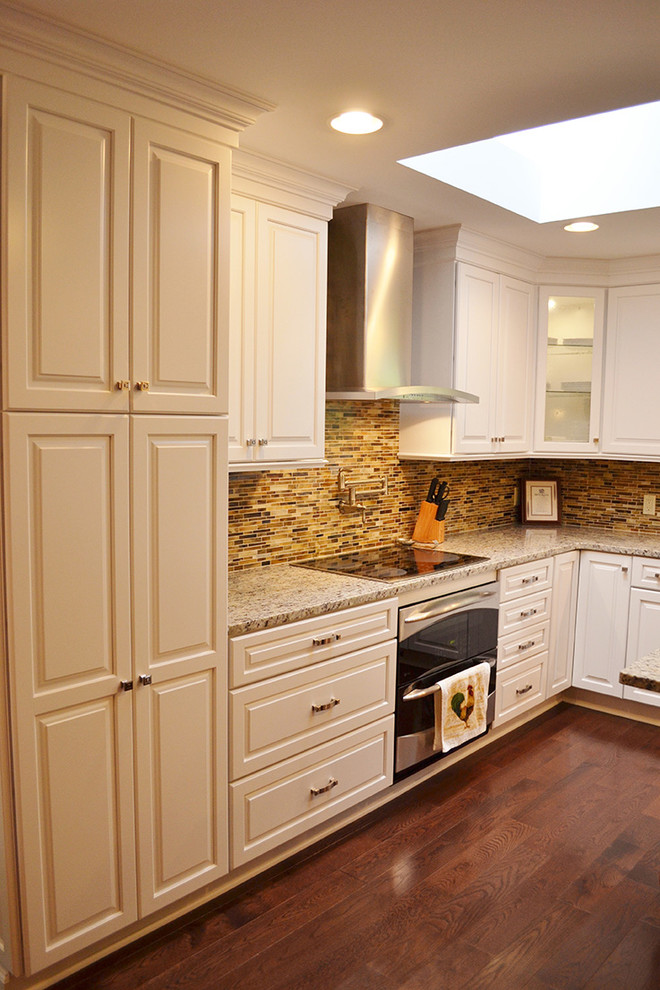 Bild på ett stort amerikanskt kök, med en undermonterad diskho, luckor med infälld panel, vita skåp, granitbänkskiva, flerfärgad stänkskydd, stänkskydd i glaskakel, rostfria vitvaror, mörkt trägolv och en köksö
