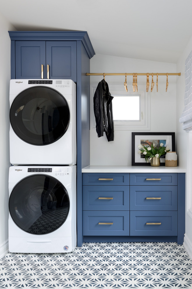 Photo of a mid-sized transitional single-wall dedicated laundry room in Toronto with shaker cabinets, blue cabinets, white walls, a stacked washer and dryer, multi-coloured floor and white benchtop.