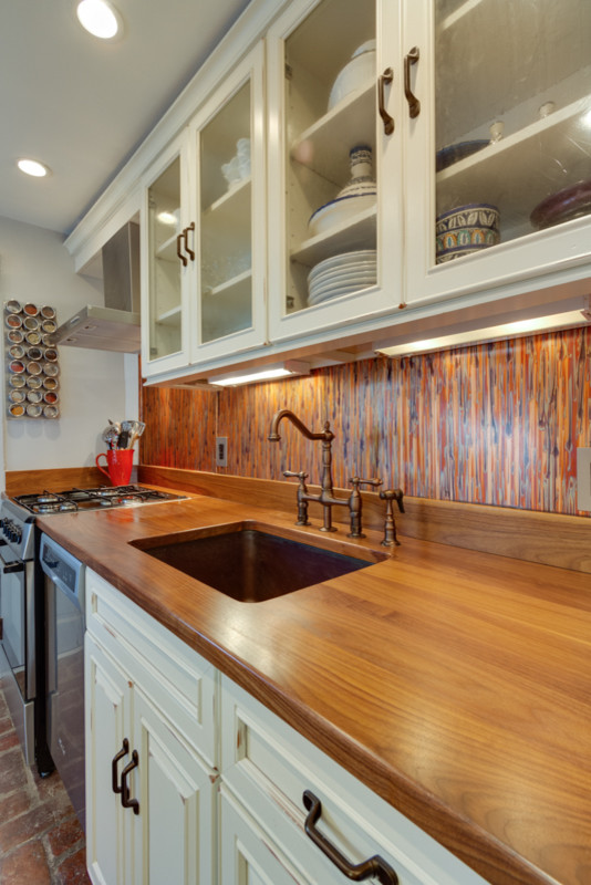 This is an example of a transitional galley eat-in kitchen in DC Metro with an undermount sink, glass-front cabinets, distressed cabinets, wood benchtops, multi-coloured splashback and stainless steel appliances.