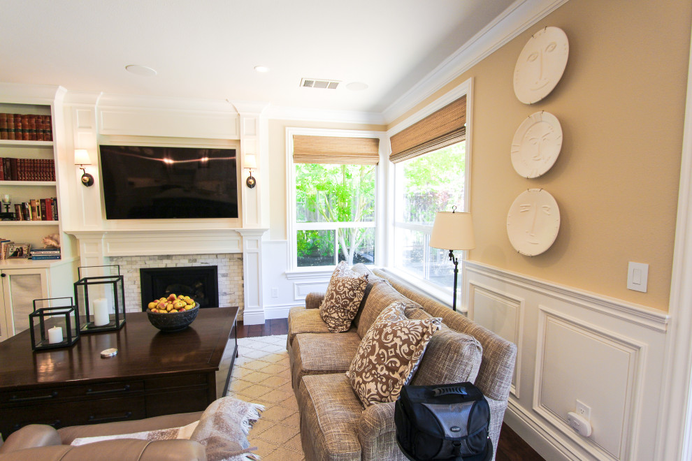 Example of a large classic open concept dark wood floor, brown floor and wainscoting family room design in San Francisco with beige walls, a standard fireplace, a stone fireplace and a wall-mounted tv