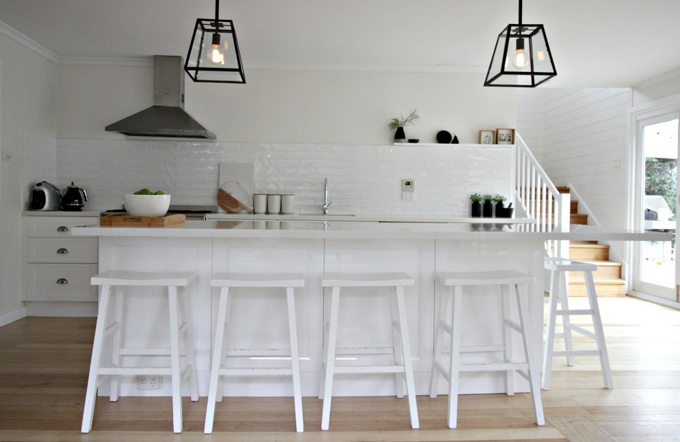 This is an example of a transitional galley open plan kitchen in Hobart with an undermount sink, white cabinets, quartz benchtops, white splashback, ceramic splashback, stainless steel appliances, medium hardwood floors and with island.