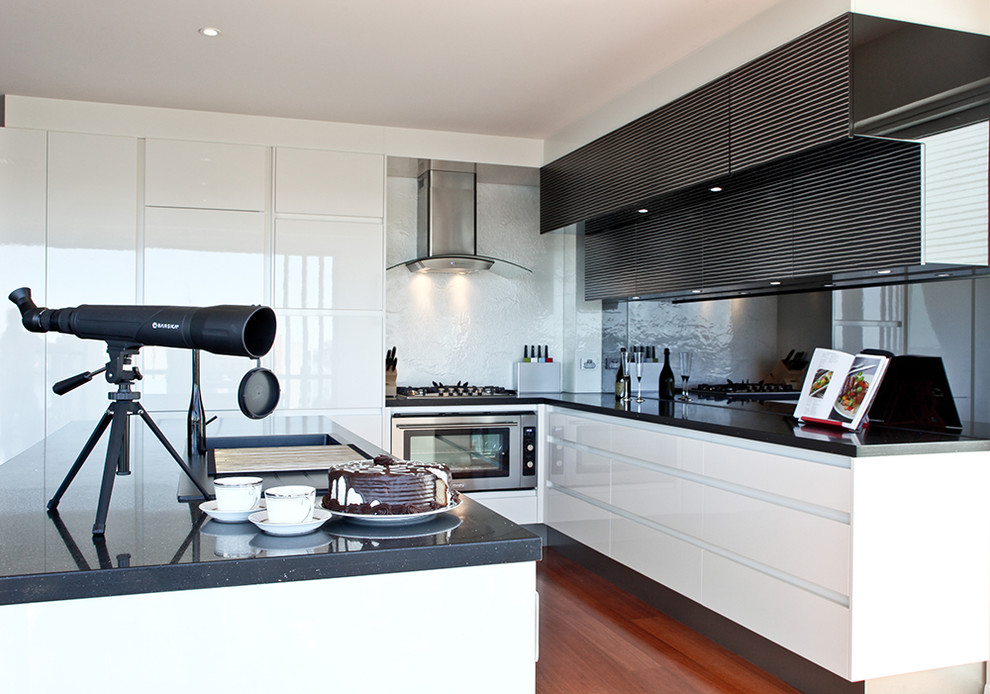 Photo of a mid-sized modern l-shaped eat-in kitchen in Brisbane with stainless steel appliances, with island, brown floor, a double-bowl sink, glass sheet splashback, flat-panel cabinets, white cabinets, quartz benchtops, metallic splashback and dark hardwood floors.