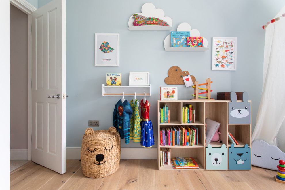 This is an example of a small contemporary gender-neutral kids' room in London with blue walls and light hardwood floors.