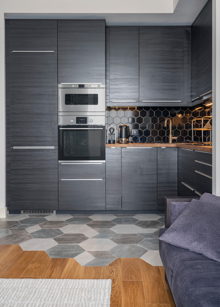 Photo of a small contemporary l-shaped open plan kitchen in Moscow with flat-panel cabinets, black cabinets, wood benchtops, black splashback, multi-coloured floor, stainless steel appliances, no island and brown benchtop.