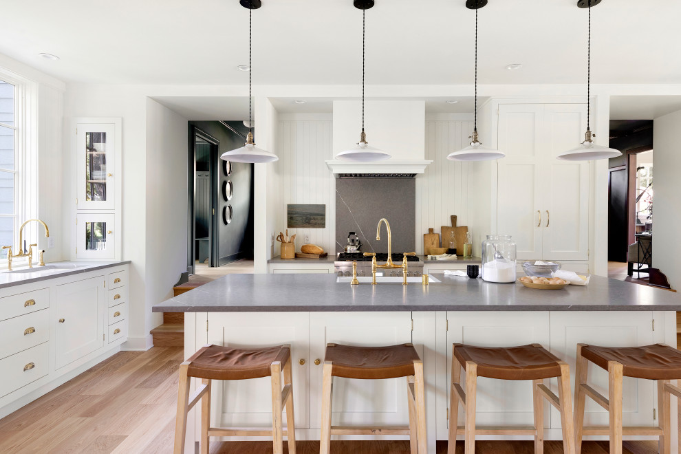 Bild på ett mellanstort lantligt grå grått kök, med en rustik diskho, skåp i shakerstil, vita skåp, bänkskiva i kvarts, vitt stänkskydd, rostfria vitvaror, ljust trägolv, en köksö och brunt golv