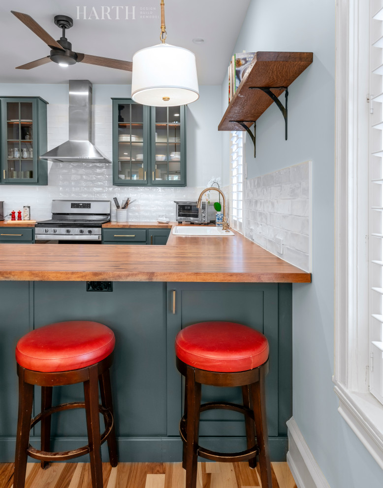 Large transitional u-shaped medium tone wood floor and multicolored floor eat-in kitchen photo in Philadelphia with a farmhouse sink, glass-front cabinets, green cabinets, wood countertops, white backsplash, ceramic backsplash, stainless steel appliances and brown countertops
