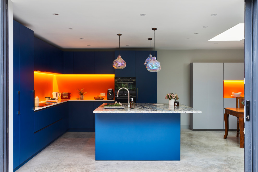 Large contemporary l-shaped eat-in kitchen in London with flat-panel cabinets, blue cabinets, quartzite benchtops, orange splashback, glass sheet splashback, stainless steel appliances, concrete floors, with island and grey floor.