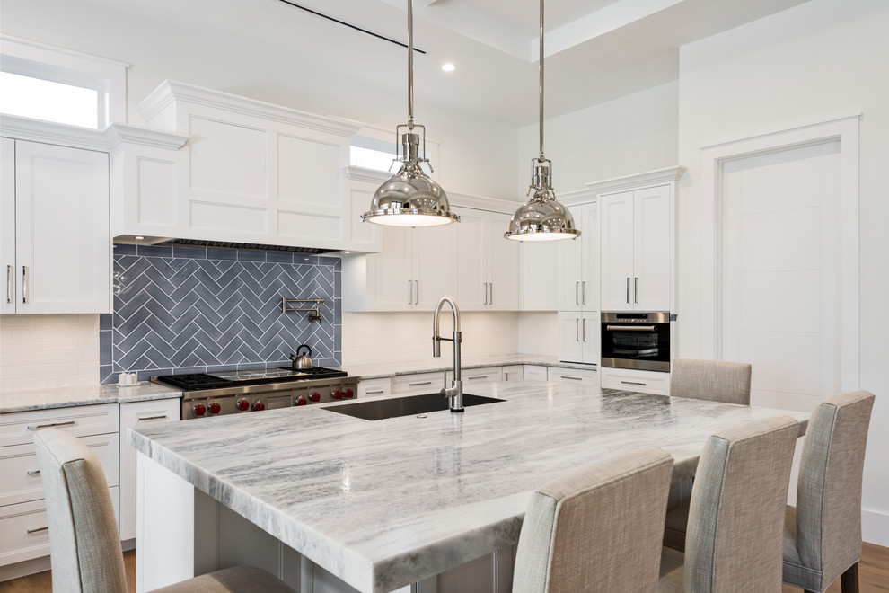 Transitional medium tone wood floor and brown floor eat-in kitchen photo in Miami with a farmhouse sink, raised-panel cabinets, white cabinets, marble countertops, white backsplash, subway tile backsplash, stainless steel appliances and an island