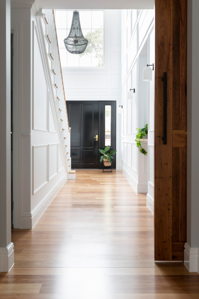 Large traditional hallway in Canberra - Queanbeyan with white walls, light hardwood floors and decorative wall panelling.