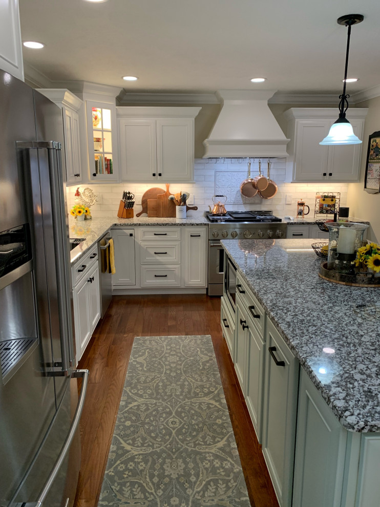 Example of a transitional l-shaped medium tone wood floor and brown floor kitchen design with an undermount sink, recessed-panel cabinets, white cabinets, granite countertops, ceramic backsplash, stainless steel appliances, an island and gray countertops