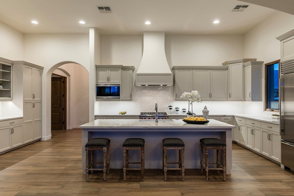 Inspiration for a large transitional l-shaped medium tone wood floor and brown floor open concept kitchen remodel in Phoenix with an undermount sink, shaker cabinets, gray cabinets, marble countertops, white backsplash, stone tile backsplash, stainless steel appliances and an island