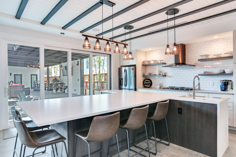 Mid-sized industrial single-wall open plan kitchen in Tampa with a farmhouse sink, shaker cabinets, white cabinets, white splashback, subway tile splashback, stainless steel appliances, cement tiles, with island, grey floor and white benchtop.