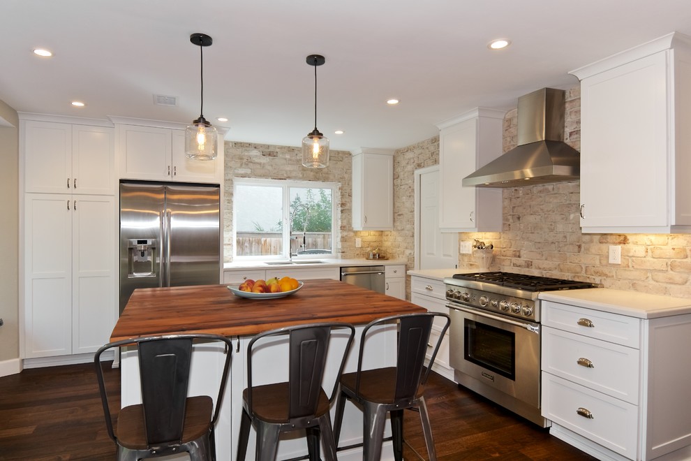 This is an example of a mid-sized country l-shaped open plan kitchen in San Diego with an undermount sink, shaker cabinets, white cabinets, quartz benchtops, white splashback, stainless steel appliances, dark hardwood floors, with island and brick splashback.