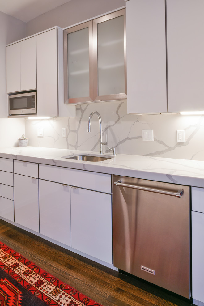 Enclosed kitchen - small eclectic galley dark wood floor and brown floor enclosed kitchen idea in Boston with an undermount sink, flat-panel cabinets, white cabinets, quartz countertops, white backsplash, stone slab backsplash, stainless steel appliances, no island and white countertops