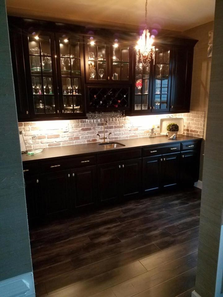 This is an example of a large traditional single-wall wet bar in DC Metro with an undermount sink, glass-front cabinets, black cabinets, laminate benchtops, red splashback, brick splashback and dark hardwood floors.