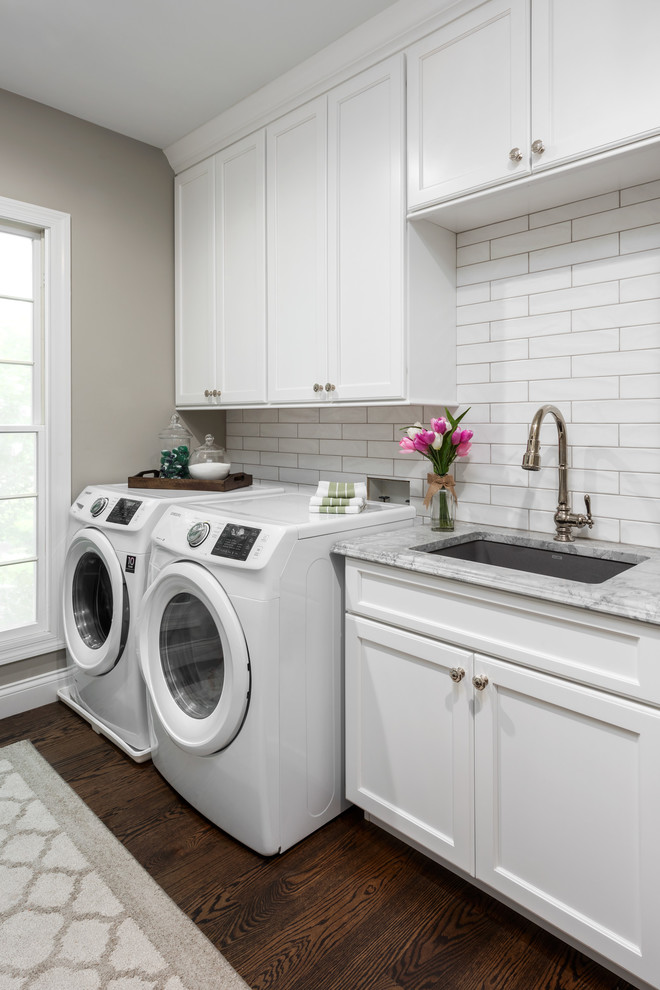 Mid-sized traditional galley utility room in St Louis with an undermount sink, flat-panel cabinets, white cabinets, quartzite benchtops, grey walls, medium hardwood floors, a side-by-side washer and dryer, brown floor and grey benchtop.