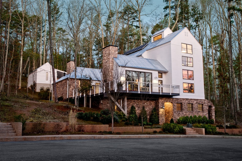 This is an example of a mid-sized country three-storey white house exterior in Atlanta with stone veneer, a gable roof and a metal roof.