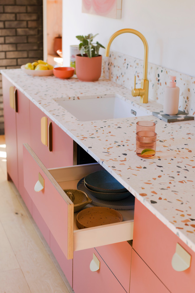 Photo of a small mediterranean single-wall open plan kitchen in Gloucestershire with a single-bowl sink, flat-panel cabinets, pink cabinets, terrazzo benchtops, multi-coloured splashback, marble splashback, light hardwood floors, no island and multi-coloured benchtop.