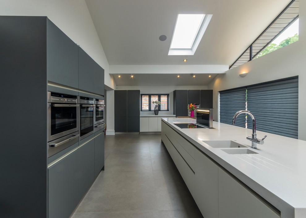 Photo of a contemporary galley kitchen in Cheshire with a double-bowl sink, flat-panel cabinets, stainless steel appliances, concrete floors and multiple islands.