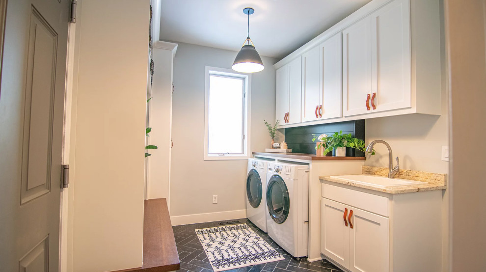 This is an example of a mid-sized transitional laundry room in Minneapolis with an utility sink, shaker cabinets, white cabinets, wood benchtops, slate splashback, slate floors, a side-by-side washer and dryer, black floor and brown benchtop.