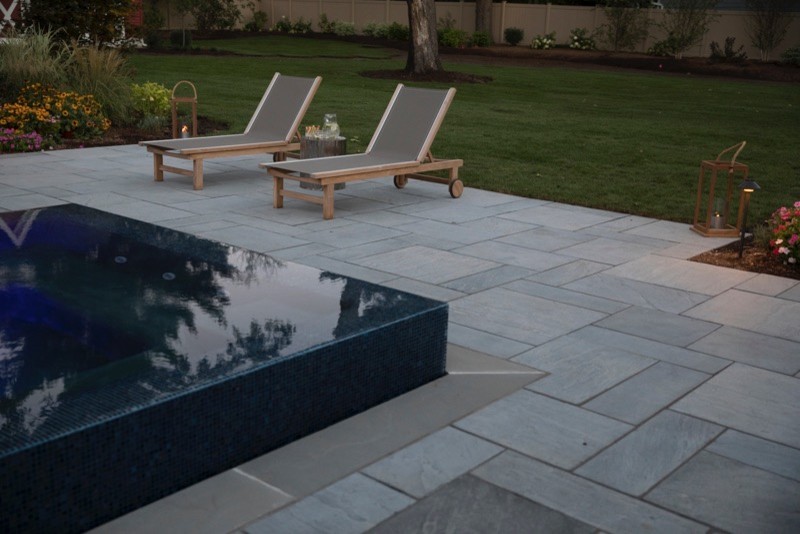 Expansive contemporary backyard rectangular lap pool in New York with a hot tub and natural stone pavers.