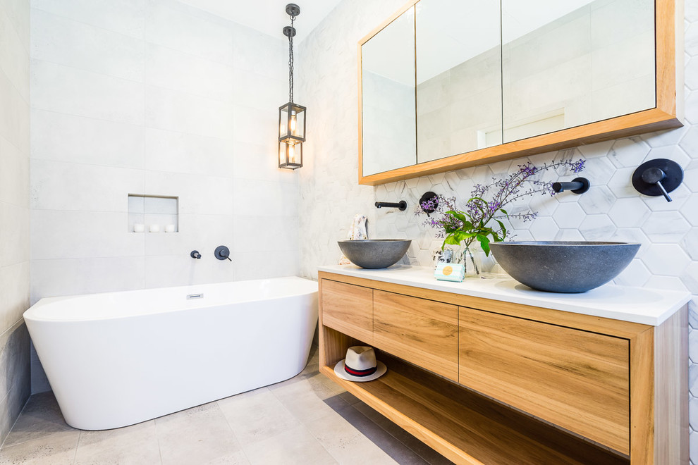Design ideas for a contemporary master bathroom in Sydney with flat-panel cabinets, medium wood cabinets, a freestanding tub, marble, grey walls, a vessel sink, beige floor and white benchtops.