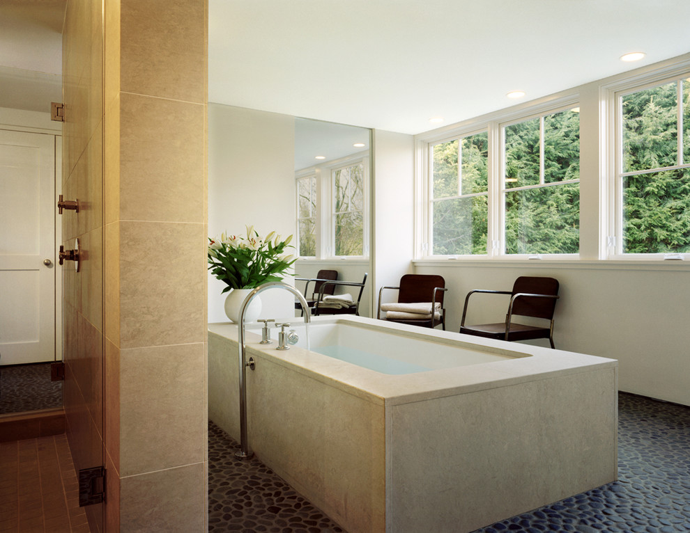Inspiration for a large contemporary bathroom in New York with an undermount tub, beige tile, stone slab, white walls and pebble tile floors.
