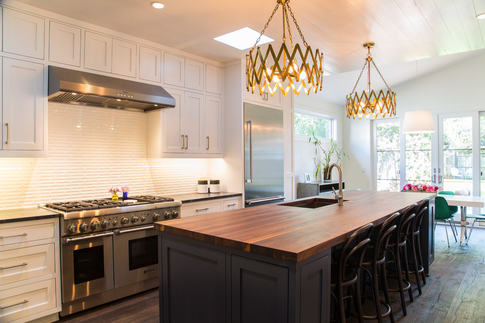 This is an example of a transitional galley eat-in kitchen in Austin with an undermount sink, shaker cabinets, white cabinets, wood benchtops, white splashback, stainless steel appliances, medium hardwood floors and with island.
