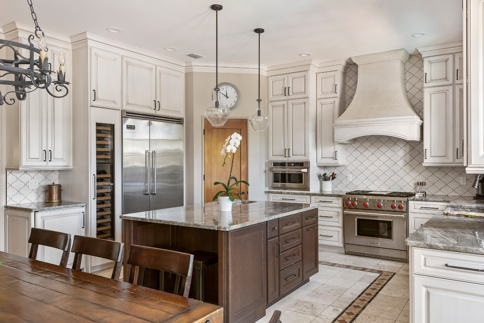 Design ideas for a large mediterranean u-shaped open plan kitchen in Tampa with a farmhouse sink, recessed-panel cabinets, beige cabinets, granite benchtops, white splashback, ceramic splashback, stainless steel appliances, ceramic floors, with island, beige floor and grey benchtop.