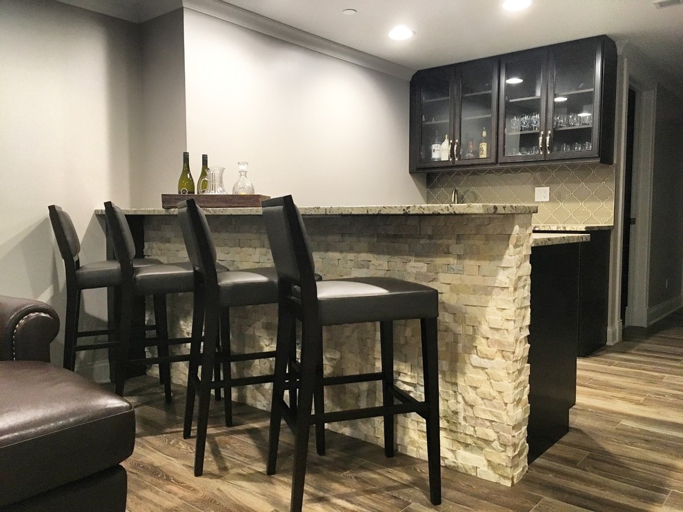 Inspiration for a mid-sized transitional single-wall seated home bar in Chicago with glass-front cabinets, black cabinets, granite benchtops, beige splashback, glass tile splashback, medium hardwood floors, brown floor and brown benchtop.