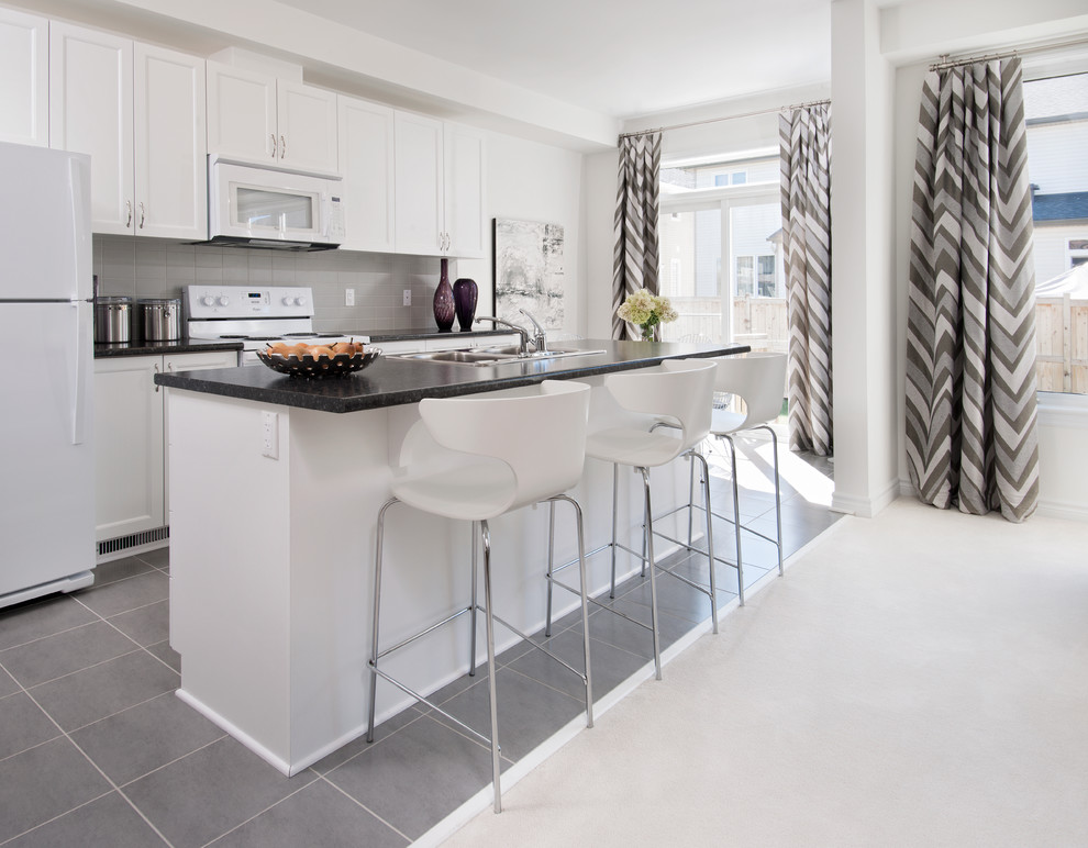 This is an example of a contemporary galley kitchen in Ottawa with a double-bowl sink, recessed-panel cabinets, white cabinets, grey splashback and white appliances.