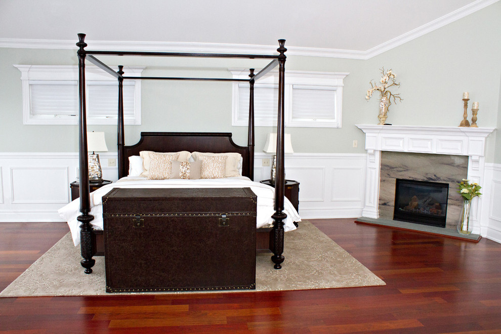 Photo of a large traditional master bedroom in New York with grey walls, dark hardwood floors, a corner fireplace, a stone fireplace surround and red floor.