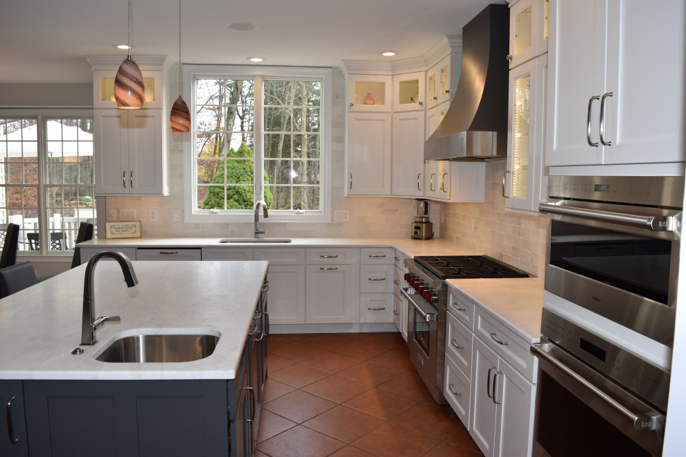 Large transitional l-shaped eat-in kitchen in Philadelphia with a drop-in sink, flat-panel cabinets, white cabinets, quartz benchtops, white splashback, subway tile splashback, stainless steel appliances, terra-cotta floors, with island, brown floor and white benchtop.