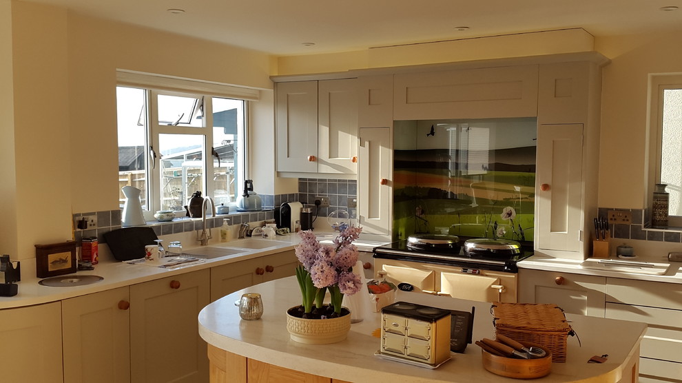 Large country u-shaped eat-in kitchen in London with a double-bowl sink, recessed-panel cabinets, beige cabinets, quartzite benchtops, multi-coloured splashback, glass sheet splashback, coloured appliances, travertine floors and with island.