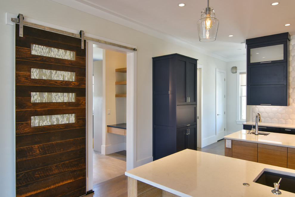 Photo of a large contemporary galley open plan kitchen in Charleston with a double-bowl sink, shaker cabinets, blue cabinets, solid surface benchtops, white splashback, ceramic splashback, stainless steel appliances, medium hardwood floors, multiple islands, brown floor and white benchtop.