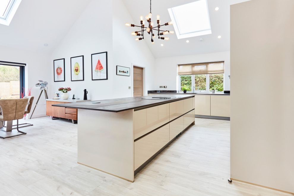 This is an example of a mid-sized contemporary l-shaped open plan kitchen in Other with an undermount sink, flat-panel cabinets, beige cabinets, quartz benchtops, beige splashback, engineered quartz splashback, black appliances, light hardwood floors, with island, beige floor, beige benchtop and vaulted.
